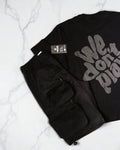 We Don't Play — Oversized Graphic Tee – Black – flat – folded black graphic t-shirt laid flat next to black cargo shorts